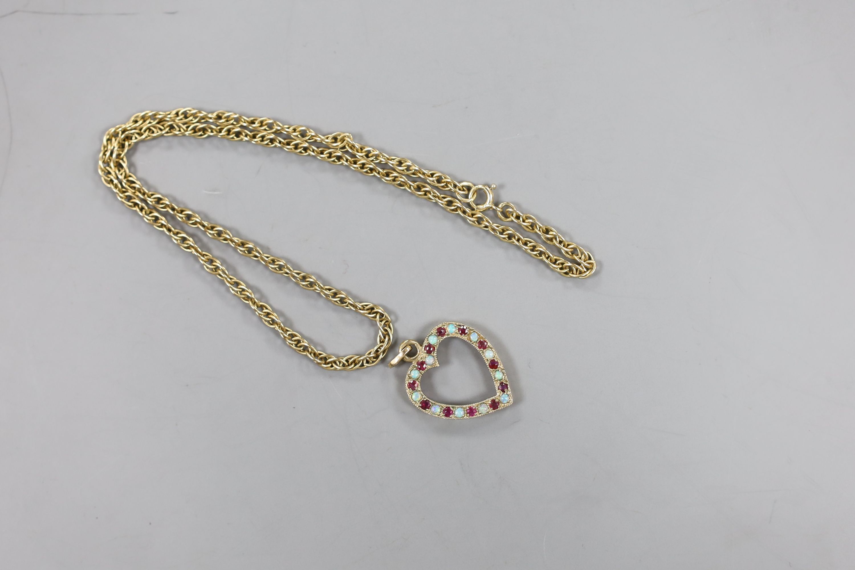 A modern 9ct gold, ruby and white opal set heart shaped open work pendant, 27mm and a 9ct gold chain, 38cm, gross weight 10.1 grams.
